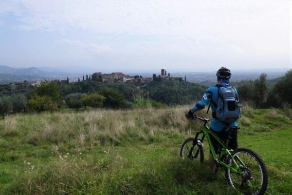 Ciclista su una collina verde che osserva un antico borgo in lontananza.